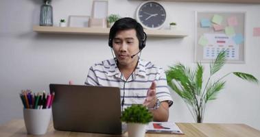 retrato de un joven agente de soporte de servicio al cliente asiático que usa auriculares mirando una computadora portátil para hacer una videollamada de conferencia de negocios por Internet.