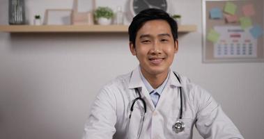 Portrait of young asian male doctor with stethoscope smiling and looking at camera. Medical assistant therapist videoconferencing. Telemedicine pandemic concept.