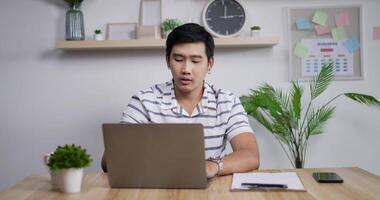 Portrait of Thoughtful Asian businessman working on laptop computer in home office. Young male manager looking on laptop screen at remote workplace. video