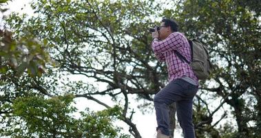 photo de dolly, jeune beau mâle asiatique à lunettes et sac à dos en randonnée sur le sentier d'une forêt verdoyante et luxuriante de haute altitude avec son appareil photo pour prendre des photos video
