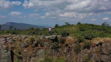 flygdrönarevy, ung vandringsman som står och reser upp händer med glad på toppen av det klippiga berget, zooma ut video