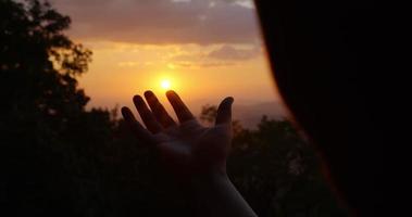 mano de hombre feliz extiende la mano al sol. la silueta de la mano sostiene el sol en la palma al atardecer video