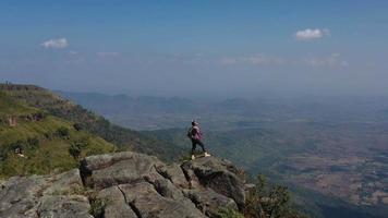 Luftdrohnenansicht, junger Wandermann, der steht und sich mit glücklichen Händen auf dem Gipfel des felsigen Berges erhebt