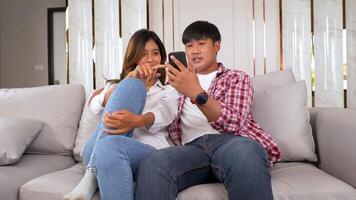 Slow motion shot, Young couple sitting on sofa in living room and use smartphone playing game together, they talk and laughing with happiness, happy family concept video