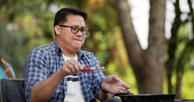 zijaanzicht van thai reiziger man bril varkensvlees steak frituren, bbq in braadpan pan of pot op een camping. buiten koken, reizen, kamperen, lifestyle concept.