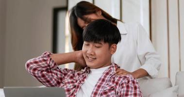 una joven y hermosa mujer asiática le estaba dando un masaje relajante a su novio que trabajaba en una computadora portátil en un sofá en la sala de estar, hablaban y sonreían con felicidad juntos video
