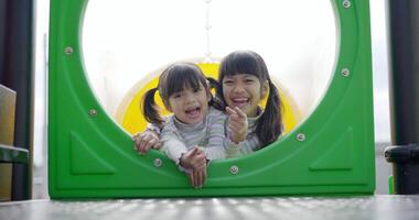 ritratto due ragazze sorelle asiatiche in slider, guardando alla fotocamera e sorridere, si divertono insieme felicemente al parco giochi video