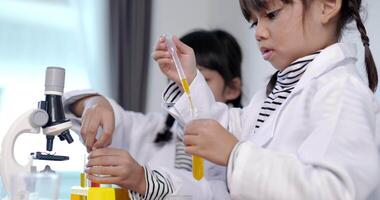 gros plan, mise au point sélective, petite fille utilise un liquide compte-gouttes sur le test du tube, deux frères et sœurs asiatiques portant un manteau apprenant à expérimenter avec des liquides, tout en étudiant la chimie scientifique video