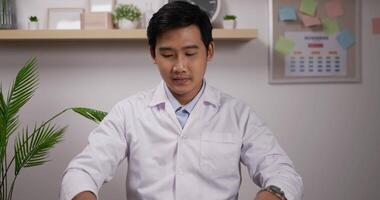 Portrait of Smiling young asian male doctor cardiologist wearing white medical coat showing stethoscope and looking at camera. Medical and health care concept. video