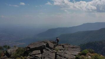 Luftdrohnenansicht, Rückansicht junger Wandermann, der mit glücklichen Händen auf dem Gipfel des felsigen Berges geht und sich erhebt video