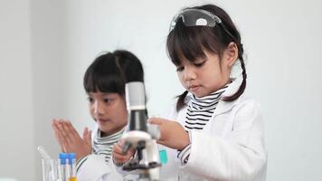 Slow motion shot, Two asian siblings wearing coat and clear glasses use microscope for experimenting with liquids, while studying science chemistry video