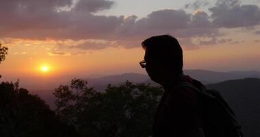slow motion bakgrundsbelyst skott, närbild bakifrån ung vandringsman står och ser sig omkring med glad på toppen av det klippiga berget i solnedgången video