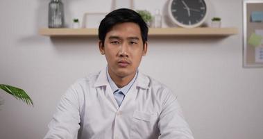 retrato de jovem médico cardiologista asiático vestindo jaleco branco e estetoscópio apontando o dedo para a câmera na clínica. conceito médico e de saúde. video