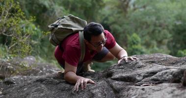 tiro em câmera lenta, jovem turista mochila homem usando óculos tentando escalar a rocha, conceito de viagem de trekking