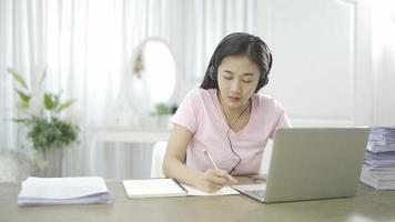 jovem asiática escola estudante universitário usar fones de ouvido aprender assistindo aula de webinar on-line webcast olhando para laptop elearning curso a distância ou professor de videochamada por webcam em casa.