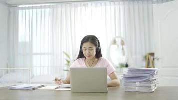 Asian young woman school college student wear headphones learn watching online webinar webcast class looking at laptop elearning distance course or video calling teacher by webcam at home.