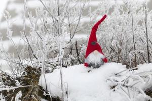 un pequeño juguete sentado en la nieve con ropa roja foto