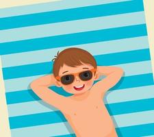 vista superior de un niño lindo con traje de baño y gafas de sol acostado en una toalla de playa divirtiéndose tomando el sol en las vacaciones de verano vector