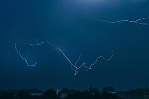 Lightning in sky over city. Bright flashes on dark night. Thunderclouds and electricity discharges in  atmosphere. photo