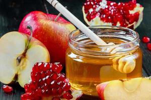 Jewish religious holiday Rosh Hashanah. Still life of apples, pomegranates and honey on dark wooden background. Traditional symbols of celebration photo