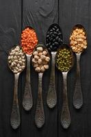 Variety of legumes in old silver spoons on a black wooden background. photo