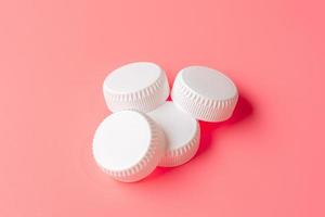 White bottles cap on light pink background. photo