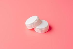 White bottles cap on light pink background. photo