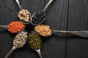 Variety of legumes in old silver spoons on a black wooden background. photo