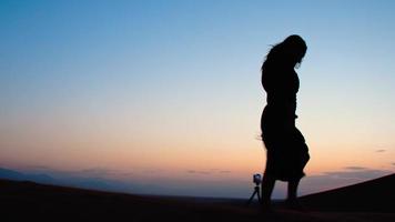 Young caucasian woman check smartphone on tripod take selfie on desert with . Travel photographer on field concept. video