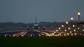 The wide bodied aircraft lands on the illuminated runway in the early morning video