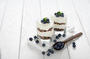Dessert with cottage cheese, fresh blueberries and granola in a glass on a white wooden background. photo