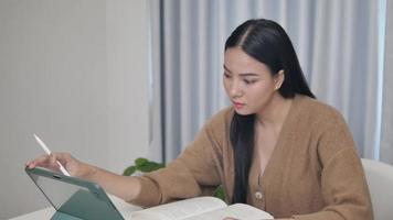 Beautiful young woman working at home in an alternative workplace with laptop computer and notebook taking notes in an indoor apartment. leisure activities women's technology activities video