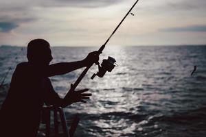 silueta hombre pescando en el mar desde el barco al atardecer. foto