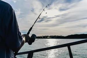 primer plano de la rueda de la caña de pescar, hombre pescando con un hermoso amanecer. foto