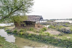 Una antigua casa de barro abandonada con techo de paja se derrumbó después de un ciclón en el campo. vista lateral de una casa de arcilla dañada. foto