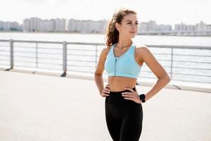 A woman does sports on the street. The trainer does exercises for stretching the body. Fitness and a healthy lifestyle. A smart watch for measuring the pulse on your hands. photo