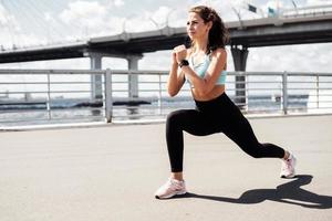 A woman does exercises on the street in the city. Cardio system training. The coach does sports in comfortable clothes. Athletics for body health. photo