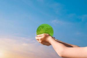 Child hands holding green earth globe over blurred sunset sky background. World environment day concept photo