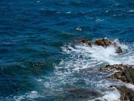 blue sea leaving white foam when crashing against the waves photo