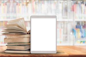 Books and tablet computer on wood table with blurred many books in library background. photo