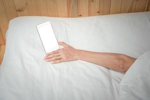 mujer sosteniendo su teléfono inteligente mientras duerme en el fondo de la cama. foto