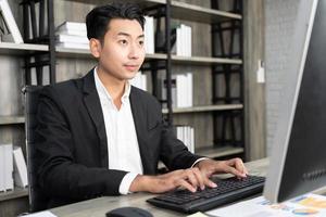 retrato de hombre de negocios usando computadora en el lugar de trabajo en una oficina. hombre de negocios positivo sonriendo mirando a la pantalla de la computadora. foto