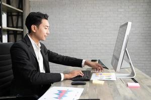 retrato de hombre de negocios usando computadora en el lugar de trabajo en una oficina. hombre de negocios positivo sonriendo mirando el papel. foto