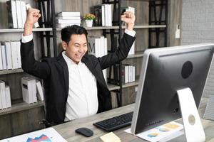 Employee employer employment entrepreneur executive man in formalwear raised hands fists up sit on chair. Emotional guy feeling glad and happy as he's great success, finishes successful business. photo