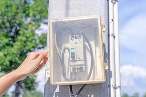 la mano del electricista humano abre o cierra la caja eléctrica en el poste eléctrico en el parque. existe un cuadro de distribución entre los jardines públicos o las calles para facilitar los remedios de emergencia en caso de corte de energía foto