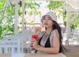 Youn beautiful and sexy Woman in Bikini with fresh juice in restaurant, smiling with happiness on vacation in summertime. Pretty smiling girl drinking tasty sweet red cocktail, amazing relaxing day photo