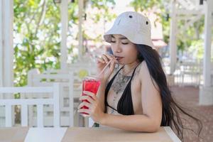 Youn beautiful and sexy Woman in Bikini with fresh juice in restaurant with happiness on vacation in summertime. Pretty girl drinking tasty sweet red cocktail, amazing relaxing day photo