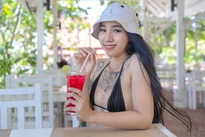 joven hermosa y sexy mujer en bikini con jugo fresco en el restaurante, sonriendo con felicidad de vacaciones en verano. chica muy sonriente bebiendo un sabroso cóctel rojo dulce, increíble día relajante foto