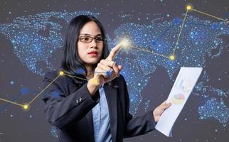 Confident businesswoman pressing a modern button on digital screen and holding bar graph sheet for trading against the stock market. Asian woman analyzed stock graph chart photo