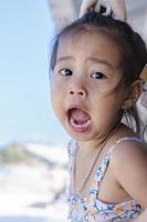 Close up of happy baby girl joy with opened mouth outdoor summer background. Little child kid girl surprised with her mother on balcony in a restaurant beside beach view on a vacation trip. photo
